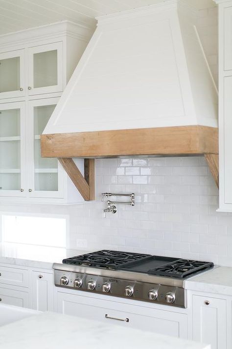 Gorgeous kitchen features a white French hood with a rustic wood trim and brackets fixed between glass front cabinets to a white subway tile backsplash framing windows positioned on either side of a Thermador cooktop fitted to inset white shaker cabinets donning a white white marble countertop. Tiny Galley Kitchen, Kitchen Hood Design, Kitchen Vent Hood, Kitchen Vent, Galley Kitchen Remodel, Kitchen Range Hood, Kitchen Hoods, Galley Kitchen, Kitchen Redo