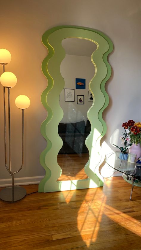 green curvy mirror (floor length) next to white globe light and glass table with vase of flowers on top. Curvy Mirrors, Curved Living Room, Pastel Room Aesthetic, Curvy Mirror, Blob Mirrors, Funky Mirrors, Funky Bedroom, Mirror Unique, Living Room Mirror