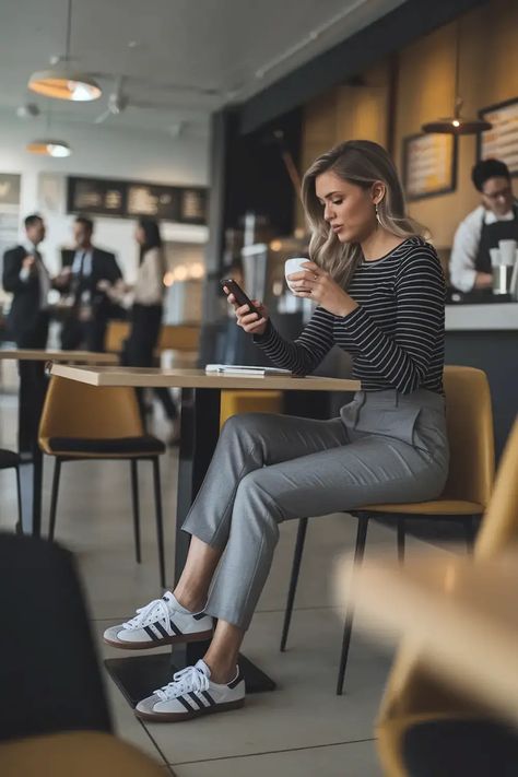 Professional checking phone in coffee shop wearing striped top and grey pants with white sneakers, sitting casually at cafe table Casual Work Outfit With Sneakers, Sneaker Office, Business Trip Outfits, Sneakers At Work, Sneakers Office, Friday Outfit Ideas, Casual Friday Outfit, Outfits With Sneakers, Work Vibes