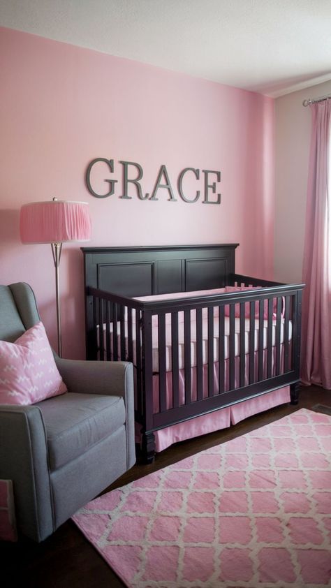 A pink nursery with soft pink walls, a black crib, a gray armchair with a pink patterned pillow, a pink floor lamp, and a patterned pink rug, creating a sophisticated and cozy atmosphere. Soft Pink Walls, Moody Nursery, Timeless Nursery, Dark Nursery, Pastel Dark, Black Crib, Nursery Designs, Name Decor, Dark And Moody