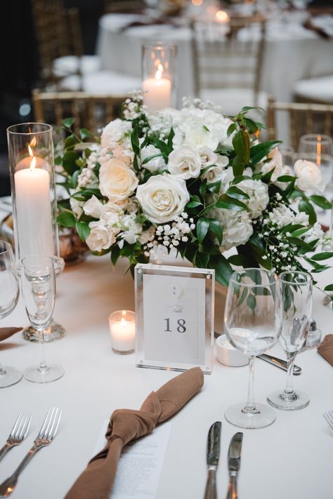 Low, lush, and classic white and green wedding centerpiece with candles to surround. Modern mocha tied napkins at each place setting. Acrylic table number frame. PC: Asya Photography https://asyaphotography.com/ Central Piece Wedding Table, Wedding Flowers White And Green Centerpieces, Wedding Centerpieces White Flowers And Greenery, Wedding Florals Green And White, Wedding Table Dressing, White And Green Wedding Table Decor, Low Wedding Centerpieces Round Table, Green And White Centerpieces Wedding, White And Greenery Centerpiece