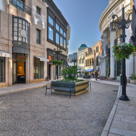 At the corner of Rodeo Drive and Wilshire Blvd, visitors are greeted by the sight of Two Rodeo Drive, a European-style shopping center complete with cobblestone walkway, street lamps and floral displays. High-end brands like Versace, Jimmy Choo, Lanvin and Tiffany & Co. can be found here. Shopping Center Architecture, Cobblestone Walkway, Rodeo Drive Beverly Hills, Mall Design, Rodeo Drive, City Design, Dream House Exterior, Luxury Shopping, Urban Planning