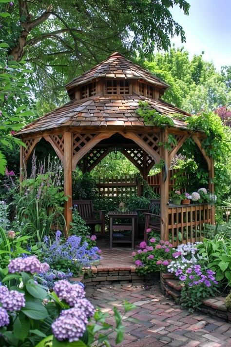 A charming wooden gazebo in a lush garden surrounded by colorful flowers and greenery, with chairs and a table under the shade. Raised Gazebo Ideas, Gazebo Garden Landscaping, Gazebo Garden Ideas, Metal Gazebo Ideas Backyard Outdoor, Small Gazebo Ideas, Covered Gazebo Ideas Backyard, Circle Pavilion, Cottage Gazebo, Pretty Gazebo