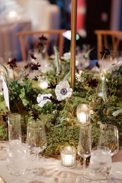 Romantic moss-covered centerpiece with white anemones, dark blooms, and sprigs of greenery, accented by flickering candles. Moss And Candle Centerpiece, Moss Candle Centerpiece, Moss Centrepiece, Moss Wedding Centerpiece, Moss Wedding Table, Moss Centerpiece Wedding, Moody Tablescape, Moss Candle, Elegant Table Decor