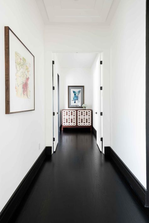 Clean crisp walls contrast against the black floors and provides the perfect backdrop to highlight the homeowner's artwork. Black Floor White Walls Living Room, Black Floor Hallway, Black Floor House, Black Floor Entryway, Black Floor White Walls, Black Floor Living Room, White Walls Black Trim, Black Floorboards, Eclectic Light Fixtures