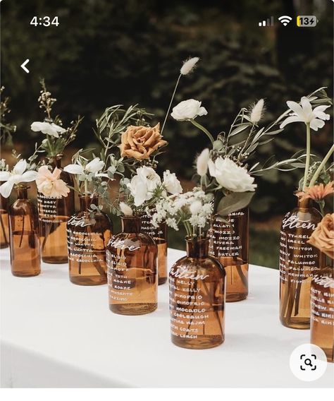 Amber Glass Vase With Flowers, Amber Glass Bottles Wedding, Glass Bottle Seating Chart Wedding, Bourbon Wedding Centerpieces, Brown Glass Bottles Wedding, Amber Jar Centerpiece, Amber Glasses Wedding Table, Glass Bottle Seating Chart, Brown Glass Wedding Centerpieces