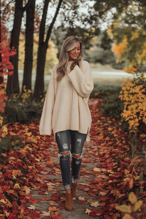 A fashionable fall outfit featuring a chunky oversized cream knit sweater, ripped jeans, and ankle boots worn by a woman walking in a colorful autumn park. Cozy Fall Sweater Outfit Ideas, Sweater Outfit Ideas, Cozy Fall Sweater, Cozy Sweaters Autumn, Fall Portraits, Oversized Knit Sweater, Sweater Outfits Fall, Chic Fall Outfits, Varsity Jackets