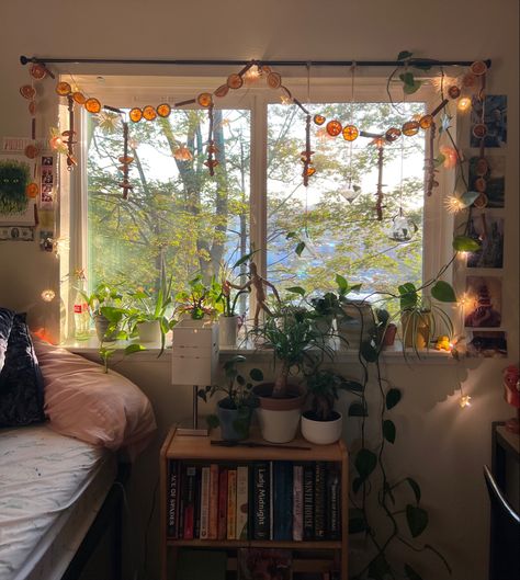 Picture of bed next to window with flower and orange garland hanging from curtain rod with plants on the windowsill. College Dorm Room Ideas Cottagecore, Earthy Dorm Room Ideas Vintage, Dorm Window Decor, Dorm Inspo Vintage, Cosy Dorm Room, Spiritual Dorm Room, Fairy Dorm Room, Cottage Core Dorm Room Ideas, Dorm Room Ideas Plants