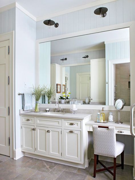 Antique sconces hang above the oversize mirror and add unexpected flair to the light and bright bathroom. The dark finish on the light fixtures adds weight to the room and helps unify the dark legs of the chair and the cabinet hardware. Their position above the vanity also provides task lighting for makeup application and grooming. Vanity With Makeup Area, Makeover Kamar Mandi, Best Bathroom Lighting, Bathroom With Makeup Vanity, Large Bathroom, Bright Bathroom, Bad Inspiration, Vanity Ideas, Master Bath Remodel