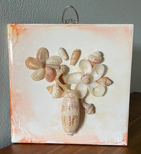 I created this floral design from shells I collected on Florida's Treasure Coast. I used an alcohol painting technique on the tile. The mix of shells used include lady slippers for the flowers, an olive shell for the vase, and various shells for accents.  The piece is finished with a protective clearcoat.  There is a corkboard backing and a heavy-duty hanger attached. You could also use a small plate holder if you don't want to hang the piece.  The piece measures 6 inches wide and 6 inches high and 1/2 inch deep. Indoor use only! Olive Shell Crafts, Shell Collection Display, Things To Do With Sea Shells, Nautical Decor Diy, Olive Shell, Alcohol Painting, Seashell Art Diy, Seashell Decor, Shell Display