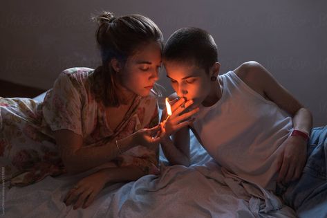 Two young women lighting a cigarette with a match while lying relaxed in bed. The light of the match illuminates their faces. Lighting Ciggerate Reference, Sharing Ciggerate, Lying In Bed Reference, Lighting Ciggerate, Lighting Ciggerate Pose, Two People In Bed, Lying On Bed Pose, In Bed Reference, Bed Reference