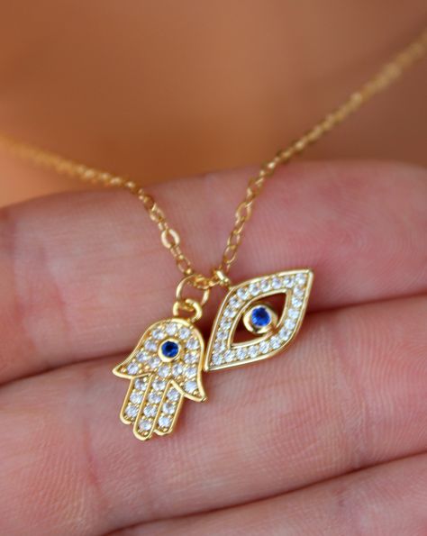 "This is a gorgeous little gold filled evil eye hamsa double charm necklace. These sparkling little charms come together on a shiny 14kt gold filled cable chain. Both charms are 14kt gold filled, have a small clear pave crystals with a blue center crystal. Hamsa measures 15x11mm and evil eye 15x8mm. PLEASE CHOSE YOUR LENGTH. These charms are even prettier in person! Comes in a cute gift box! Model is wearing a 16\" length in photo. This listing is for the double pendant necklace only. Shown with Gold Evil Eye Necklace, Hamsa Necklace Gold, Floral Henna, Evil Eye Hamsa, Creative Jewelry Photography, Hamsa Jewelry, Evil Eye Necklace Gold, Gold Hamsa, Hamsa Necklace