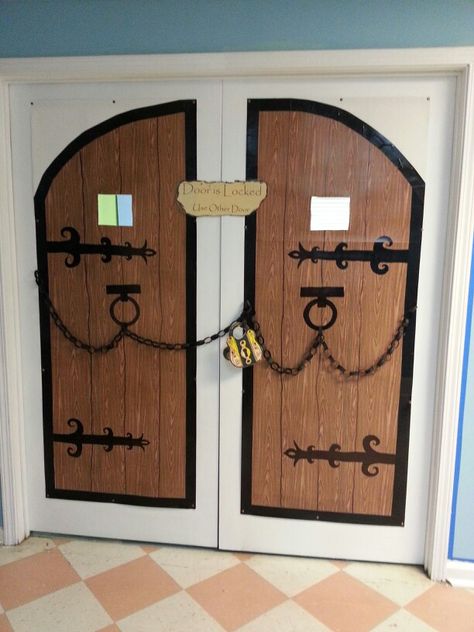 For castle theme classroom - castle doors are made from poster board covered with wood grain Contact Paper and black duct tape. The hinges are drawn on with permanent markers. And then I added paper chains and a lock because these doors are locked. Castle Classroom Door, Classroom Castle, Medieval Classroom, Medieval Theme Party, Keepers Of The Kingdom Vbs, Mighty Fortress Vbs, Castle Theme Classroom, Medieval Chandelier, Castle Classroom