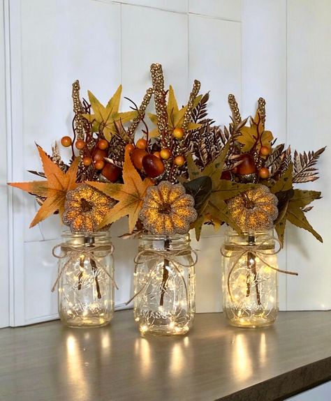 These fall lighted mason jar centerpieces are a perfect addition to your fall decor! They would make a great Thanksgiving centerpiece. Also ideal for a fall wedding or fall bridal shower.  Mason Jars are Ball Regular Mouth Pint Size jars.  Each floral arrangement will include a faux fall arrangement with a glitter covered pumpkin pick and a gold leaf pick.  A piece on twine will be tied to the top of each jar. And a 7ft set of warm white fairy lights will be included for each jar if purchase whe Fall Wedding Outdoor Decorations, Mason Jar Centerpieces Fall, Fall Vase Filler Ideas, Lights In Jars, Fall Decor Outside, Gold Fall Wedding, Fall Mason Jar Centerpieces, Fall Centerpiece Ideas, Simple Thanksgiving Table Decor