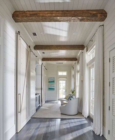 Floor to ceiling shiplap paneling with reclained wood beam. This hallway boasts rustic wood beam ceiling, shiplap walls, shiplap ceiling as well a wall of French doors and transom windows dressed in white cotton curtains. A chic hall boasts a nook filled with a blue wet bar flanked by rooms finished with pecky cypress barn doors on rails. #shiplap #reclaimedwood #floortoceilingshiplap floor-to-ceiling-shiplap-paneling-with-reclaimed-wood-beam: Shiplap Paneling, Florida Beach House, Shiplap Ceiling, Wood Beam Ceiling, Long Hallway, Beach House Interior, Beach House Design, Style Deco, Exposed Beams