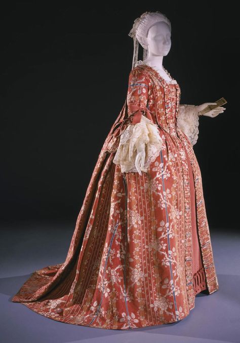 This is a woman's dress known as a Robe à la française, otherwise known as a sack-back gown. This style of gown had fabric at the back arranged in box pleats which fell loose from the shoulder to the floor with a train. This particular robe à la française was made with a silk taffeta with woven ribs and supplementary weft flosses, silk looped fringe and displayed a floral pattern. In the front, the gown was open, showing off a decorative matching stomacher and petticoat . 1740s Dress, 1760s Fashion, 1700s Clothing, 1700s Dresses, Historic Dresses, Georgian Dress, 18th Century Dresses, 18th Century Gown, 1700 Fashion