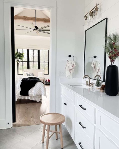 Light wood stool stands on a gray herringbone tile bathroom floor in front of a white vanity. The vanity is paired with a rectangular black frame mirror lit by a brass and glass vanity light. Light Gray Floor Bathroom, Grey Herringbone Tile Bathroom, Gray Herringbone Tile Floor, Herringbone Tile Bathroom Floor, Gray Herringbone Tile, Herringbone Tile Bathroom, Tile Bathroom Floor, Black Frame Mirror, Herringbone Tile Floors