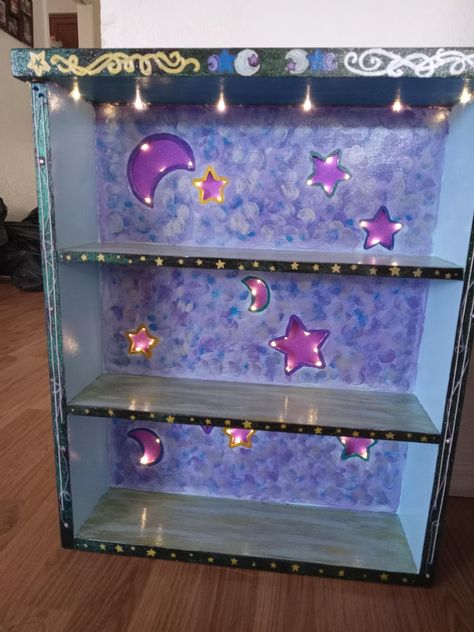 Medium sized bookshelf with star and moon cut-outs, illuminated with battery operated fairy lights inset behind a purple glittery back. Has three shelves, perfect for books, knick-knacks, or framed photos to name a few! Perfect for a babys nursery, or even your own bedroom! Star Shelf, Moon And Stars Furniture, Purple Fairy Bedroom, Fairy Core Bookshelf, Purple Fairy Nursery, Fairy Shaped Shelf, Purple Moon And Stars Nursery, Moon And Stars Fairy Lamp, 50s House