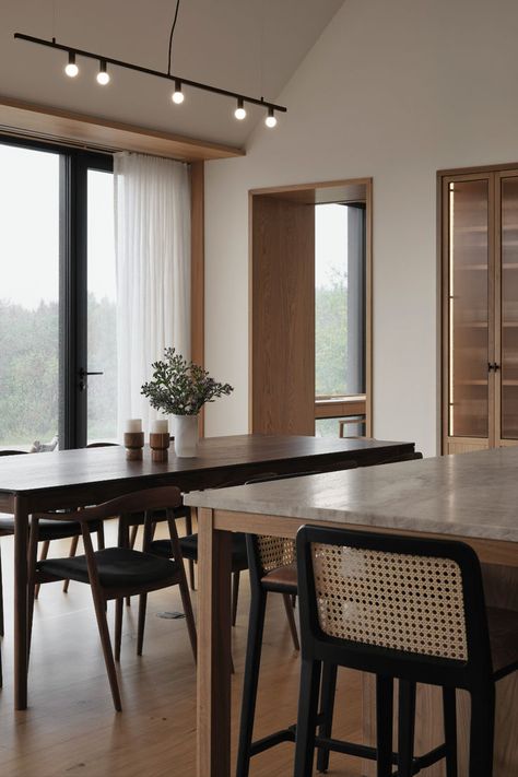 Minimalist dining area featuring a wooden table, black chairs, and natural light from floor-to-ceiling windows. Black Cedar House, Minimalist Dining Area, Sleek Chairs, House On The River, Cedar House, Cedar Homes, Wooden Floors, Floor To Ceiling Windows, Wooden Dining Tables