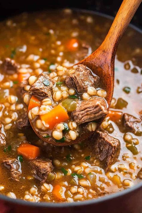 A close-up shot of a wooden spoon scooping beef barley soup from a pot. The soup is rich and thick with chunks of tender beef, whole barley grains, diced carrots, and finely chopped herbs, showcasing a hearty and nutritious meal. Crockpot Beef Barley Soup, Beef And Barley Stew, Beef Barley Stew, Beef And Barley Soup, Thanksgiving Crockpot Recipes, Slow Cooker Stew Recipes, Barley Stew, Beef And Barley, Beef Barley