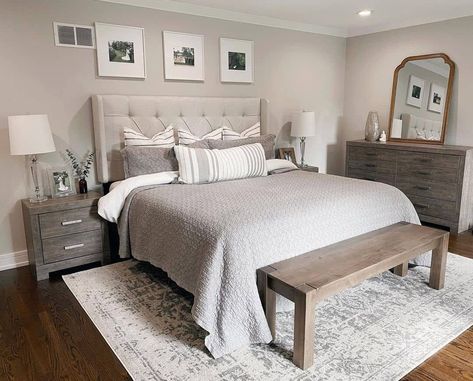 A neutral primary bedroom with beige walls and white trim holds a large bed with an upholstered headboard. A textured beige quilt covers the bed with striped accent pillows on top. A farmhouse bend sits at the foot over a gray and white rug. Weathered nightstands sit on each side of the bed holding lamps, framed photos, and plants, and a matching vanity stands nearby with decor and a vintage mirror...   Image: laurenashleyhansen Hannah House, Floor Bedroom Ideas, Light Gray Bedroom, Bohemian Bedroom Design, Cozy Bedroom Design, Grey Bed Frame, Grey Bedroom Decor, White Bed Frame, Chic Bedroom Decor