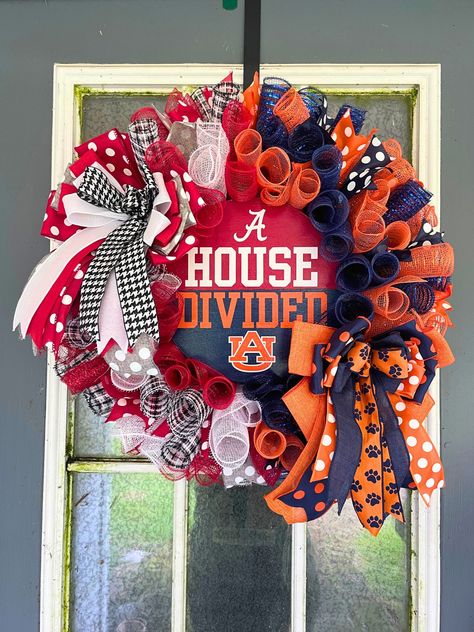 Showcase your spirited household rivalry with this unique "House Divided" wreath! This handcrafted wreath perfectly blends the crimson and white colors of the University of Alabama and orange and navy blue of the Auburn Tigers.  This beautiful, handcrafted wreath is made with high quality deco mesh and wired ribbon, and a hand painted centerpiece sign. The sign was painted with acrylic paint and lettering was made with vinyl; it is coated in multiple layers of mod podge to prevent the paint from House Divided Football Wreath, House Divided Football Sign, Alabama Football Wreath, House Divided Football, Alabama Crafts, House Divided Wreath, Alabama Wreaths, Sports Crafts, Christmas Bazaar