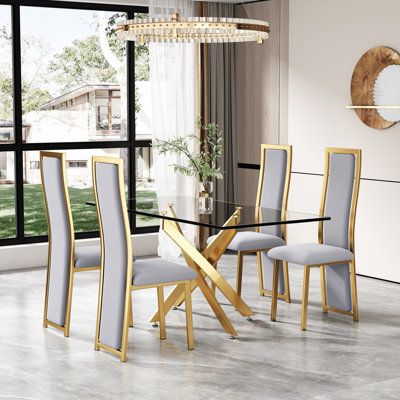 Modern Dining Room Dining Table Set, this dining table set features a tempered glass table top that provides plenty of room for 4 people to comfortably dine together. The crystal clear glass table top pairs perfectly with the sleek and stylish X-shaped gold metal legs to create a visually stunning centerpiece for your dining room. Chair Color: Gray/Gold | Mercer41 Bloomsdale 5 - Piece Glass Top Pedestal Dining Set 30.0 H x 31.5 W x 63.0 D in Metal in Gray / Gold | Wayfair Room For 4 People, Blue Dining Room Decor, Dine Together, Clear Glass Table, Dining Table Gold, Gold Dining, Dining Room Blue, Dinning Set, Tempered Glass Table Top