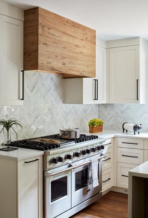 White and gray marble herringbone wall tiles hold a reclaimed wood range hood between white shaker upper cabinets finished with oil rubbed bronze pulls. Reclaimed Cabinets, Herringbone Wall Tile, Vintage Modern Kitchen, Backsplash White, Farm Style Kitchen, Kitchen Hood Design, Wood Range, Marble Herringbone, Tiles Backsplash