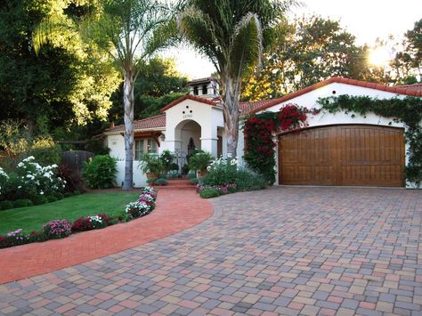 This Spanish Colonial Revival house with a barrel tile roof features a paver driveway, sidewalk and a wooden, arched garage door surrounded by bougainvillea. A mission parapet on top of the roof adds to the home's eclectic look. Colonial Revival House, Spanish Style Decor, Spanish Colonial Homes, Mediterranean Exterior, Spanish Decor, Mediterranean Home Decor, Spanish Style Home, Casas Coloniales, Hacienda Style