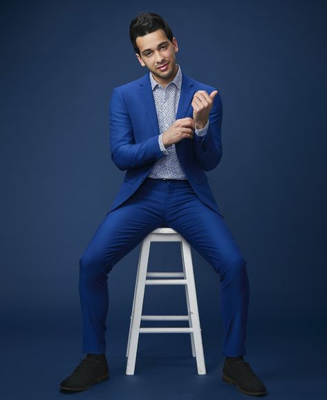 Male model in a blue suit on a blue background sitting on a white stool. Male Suit Poses, Chair Poses Photography Men, Chair Photoshoot Posing Ideas Men, Poses For Boys Photoshoot, Birthday Shoot Ideas For Men, Man Leaning Back In Chair Pose, Male Model Suit Photoshoot, Male Model Photoshoot Ideas, Blue Background Photoshoot