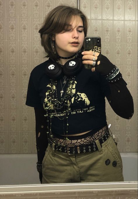 A mid-sized person/girl wearing a    black cropped graphic shirt, wide brown cargo shorts, black skull headphones, black cobweb tights, platform dr. Martens and multiple dark green and gray crystal rings and bracelets. 		The person is also wearing multiple silver necklaces. Masc Necklaces, Goth Maximalism Fashion, Painted Headphones, Crowcore Outfit, Fit Aesthetic Outfit, Enby Outfits, Maximalism Fashion, Metalhead Fashion, Headphone Outfit