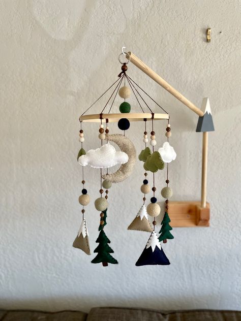 "This fun felt custom mobile features a subtle color palette of neutrals with navy and green, accented with light and dark wooden beads, and a few felted wool balls. Every plush felt decoration is hand stitched in coordinating embroidery thread to create more texture and dimension within the mobile. A sandstone moon hangs from the middle of the mobile, surrounded by pillowy clouds. Evergreen trees and snow capped mountains in Navy, Latte, and Toffee dangle towards your little adventurer. This is Neutral Green Nursery, Navy Baby Room, Mountain Nursery Theme, Felt Mountain, Green Nursery Boy, Navy Blue Nursery, Monochromatic Blue, Forest Nursery Decor, Woodland Mobile