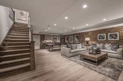 A finished basement with a rustic straight staircase and hardwood flooring. The brick wall adds style to the room. French House Plans, Finished Basement Designs, Basement Decoration, Architecture Renovation, Dream Basement, Rustic Basement, Basement Layout, Modern Basement, Basement Inspiration