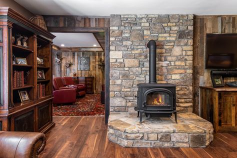 Stone accent, wood stove, and rustic hard wood flooring in a basement remodel by Judd Builders. Wood Stove Basement Ideas, Wood Stove In Basement, Wood Burning Stove Basement, Brick Wall Wood Stove, Stone Hearth Ideas, Basement Wood Stove, Basement With Wood Stove, Log Cabin Wood Stove, Stone Hearths With Wood Stoves