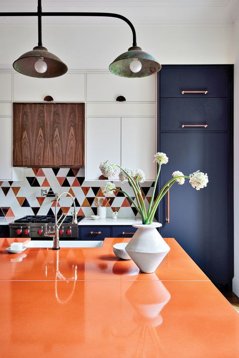 Orange accents distinguish the kitchen, from the island’s lava stone countertops from Ranieri Lava Stone, to the Mercury Mosaics triangle tile backsplash. A custom walnut range hood by Mason Woodworks LLC and a vintage industrial light from 1stdibs establish subdued hues. Orange Backsplash Kitchen, Walnut Range Hood, Orange Countertops, Midcentury Tile, Orange Kitchen Designs, Unique Kitchen Backsplash Ideas, Triangle Tile, Creative Kitchen Backsplash, Backsplash Inspiration