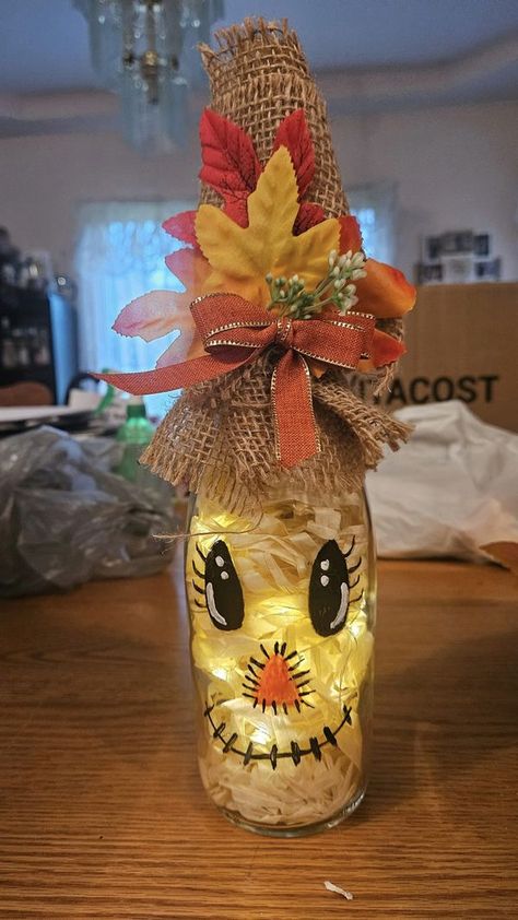 Crafty Fun Group | I took off the label and filled a wine bottle with a Hawaiian skirt cut up and put lights with a cork from Amazon | Facebook Wine Bottle Witches, Wine Bottle Scarecrow With Lights, Fall Bottle Crafts, Scarecrow Wine Bottle Craft, Wine Jug Crafts, Halloween Wine Bottle Crafts, Thanksgiving Wine Bottle, Fall Wine Bottles, Halloween Wine Bottles