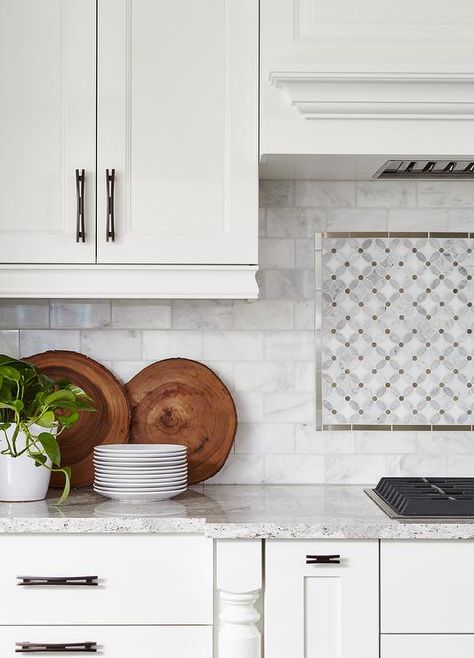 A white wood panel hood is fixed to marble subway backsplash tiles framing mosaic  marble cooktop tiles positioned over an integrated gas cooktop. Kitchen Backsplash Behind Stove, Backsplash Behind Stove, White Beveled Subway Tile, Stove Decor, White Wood Paneling, Kitchen Cooktop, Subway Backsplash, Kitchen Countertop Decor, Countertop Decor