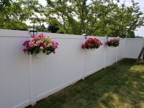 A beautiful back yard with fence hangars. Backyard Fence Before And After, Side Of Fence Landscaping, Vinyl Fence Ideas Front Yard, White Fence Decorating Ideas, Colored Fence Ideas, Along Fence Landscaping Backyards, Potted Plants Along Fence, Flowers On Fence Ideas, White Fence Backyard Landscaping