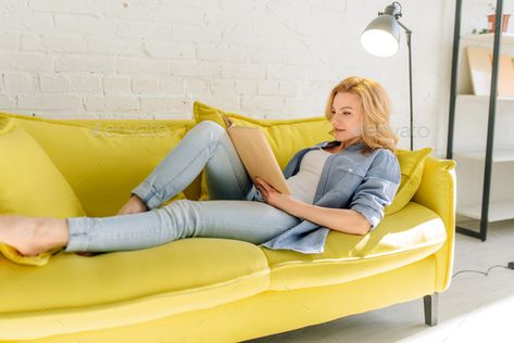 Young woman lying on cozy yellow couch and reading a book, living room in white tones on background. Attractive female person with magazine sitting on sofa at home Reading A Book Pose, Book Pose Reference, Art Base Pose, Book Living Room, Book Pose, Sitting Pose Reference, Yellow Couch, Packing Travel, Woman Laying