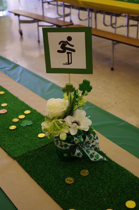 Track and FIeld Banquet centerpieces. Floral centerpieces were added this year and so we just added our Pictogram.  Faux grass runners and chocolate coins add texture. Track Banquet Centerpieces, Track And Field Banquet Ideas, Auction Centerpieces, Track Banquet, Sports Banquet Centerpieces, Men's Ministry, Swim Banquet, Field Party, Beer Decor