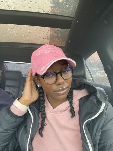 She has curly hair braided into two braids. She is sitting in car wearing a pink hoodie and pink baseball cap. Braids And Baseball Caps Black Women, Braids Headband Hairstyle Black Women, Baseball Hat Curly Hairstyles, Cap With Braids Black Women, Low Bun With Hat Black Women, Hats And Braids Black Women, Visor Hat Hairstyles Black Women, Natural Hair Baseball Cap, Natural Hairstyles With Hats