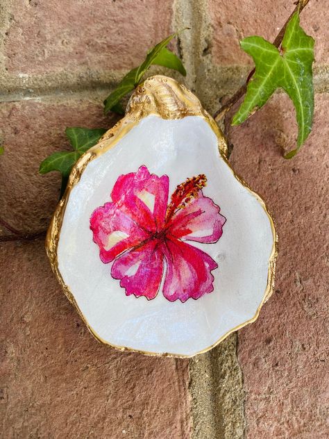 Oyster Trinket Dish - The shell is hand-painted and decoupaged with a beautiful Hawaiian 🌺 flower design. Also, each shell has an added clear coating for protection and shine. Each shell is personally handpicked to create this gorgeous trinket dish with gilded trim. The finished look includes an iridescent finish on the bottom. Approximate size 3.5" The perfect  jewelry holder or decorative piece to add a touch of the coast to any home or office.  This item has been carefully handcrafted to cre Painted Shell Jewelry Holder, Hawaiian Flower Design, Shell Jewelry Holder, Painted Sea Shells, Painting Shells, Shell Painting, Shell Trinket Dish, Hawaiian Gifts, Birthday Painting