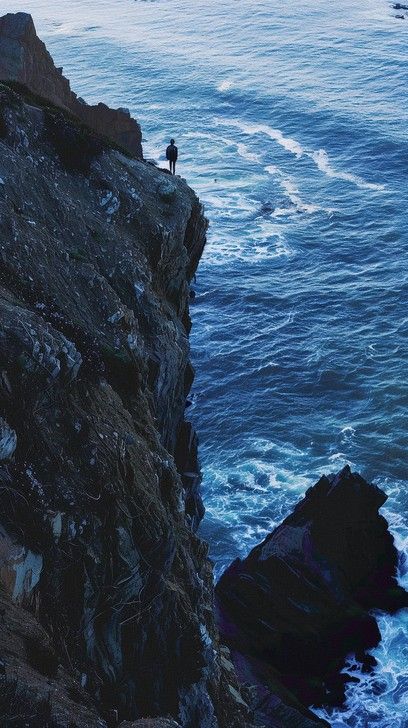 A lone adventurer stands at the edge of a towering cliff overlooking the vast, mesmerizing ocean. Cliffside Aesthetic, Standing On A Cliff, Cliff Edge, People Pictures, Inheritance Games, Cliff House, Call Of The Wild, Beach Rocks, Image Downloads