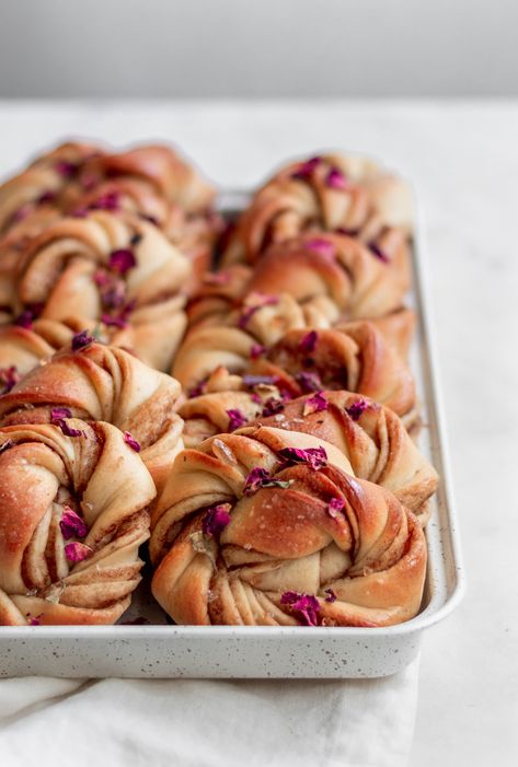 These rose cardamom buns remind me of traveling through Sweden! Cardamom buns (a.k.a. Kardemummabullar) are the Swedish version of a cinnamon bun, but even better because they have a floral, cardamom-brown sugar filling! We also add rose syrup to complement the floral flavors in these rolls. As beautiful as they are, they are a surprisingly easy homemade bread recipe that is perfect with coffee or tea for fika. I like serving them for breakfast or brunch as well. They are a huge crowd-pleaser! Swedish Cardamom Buns Recipe, Cardamom Buns Recipe, Swedish Cardamom Buns, Breakfast Buns, Sara Lynn, Rose Syrup, Cardamom Buns, Baking Buns, Homemade Bread Recipes Easy