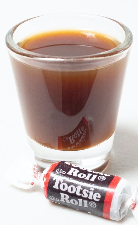 A shot glass filled with a brown tootsie roll shot on a white background next to a piece of tootsie roll candy. Tootsie Roll Drink, Circus Drinks, Tootsie Roll Shot, Mixology Recipes, Spring Drink, Cocktail Shots, Two Ingredient, Non Alcoholic Cocktails, Tootsie Roll