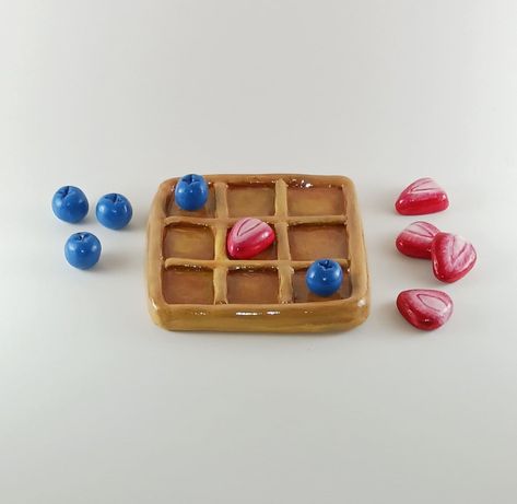 "Waffle Tic-Tac-Toe Board with Strawberry and Butter cube game pieces: Fashioned with oven-baked clay, hand-painted with acrylic paints, and sealed with Triple Thick glaze gloss for safe measure! 10 game pieces altogether: 5 strawberry slices, 5 cubes of blueberries (all game pieces vary in size between an inch to two inches). Gameboard: 4.5\" x 4.5\" and sits 3/4\" tall Weighs approximately 9 lbs. 2 ounces" Clay Tic Tac Toe Board Ideas Cute, Diy Tic Tac Toe Board, Waffle Tic Tac Toe Board, Oven Baked Clay Ideas, Oven Bake Clay Ideas, Clay Tic Tac Toe Board, Clay Tic Tac Toe, Breakfast Nook Decor, Strawberries And Blueberries