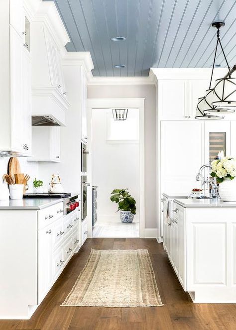 A Grosvenor Linear Triple Pendant hangs from a blue plank ceiling over a white kitchen island boasting a farmhouse sink and a polished nickel gooseneck faucet mounted to a gray countertop. Shiplap Ceiling, Plank Ceiling, Blue Ceilings, Grey Countertops, White Kitchen Island, Pot Lights, Colored Ceiling, Kitchen Ceiling, Farmhouse Dining Room