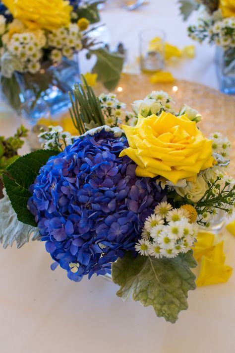 Centerpieces kept with the blue and yellow color palette and included arrangements of yellow roses, blue hydrangeas and white asters. Wedding Flowers Blue Hydrangea, Blue Hydrangea Centerpieces, White Hydrangea Centerpieces, Blue Yellow Weddings, Yellow Rose Bouquet, Yellow Hydrangea, Hydrangea Bouquet Wedding, Yellow Wedding Flowers, Hydrangea Centerpiece