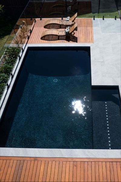 A pool with mid grey coping and surrounds and a dark water colour, with timber pool deck. Dark Blue Pool, Pool Pavers, Dream Backyard Pool, Paver Tiles, Stone Pool, Dark Water, Pool Tiles, Blue Pool, Pool Coping