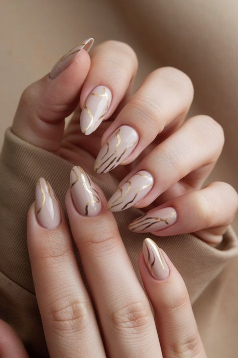 The photo shows a hand with medium-length almond-shaped nails painted in a soft nude colour with gold detailing. The simple and glossy finish gives the manicure a clean and elegant appearance. Abstract Almond Nails, Almond Shape Nail Designs, Almond Shaped Nails Designs, Glitter Gradient Nails, Almond Nail Designs, Sophisticated Nails, Shiny Nails Designs, Nailinspo Nailart, Line Nail Art